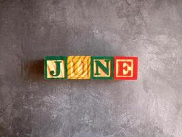 A photo of a wooden block with the words june written on it, styled in isolation with space for text.