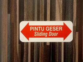 A photo of a sign that says Sliding Door, set against a wooden background.