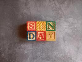 A photo of a wooden block with the words sunday written on it, styled in isolation with space for text.