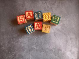 A photo of a wooden block with the words saturday written on it, styled in isolation with space for text.
