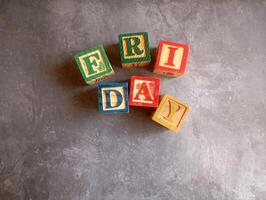 A photo of a wooden block with the words friday written on it, styled in isolation with space for text.