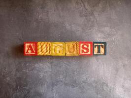 A photo of a wooden block with the words august written on it, styled in isolation with space for text.