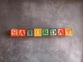 A photo of a wooden block with the words saturday written on it, styled in isolation with space for text.