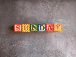 A photo of a wooden block with the words sunday written on it, styled in isolation with space for text.