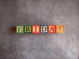 A photo of a wooden block with the words friday written on it, styled in isolation with space for text.