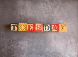 A photo of a wooden block with the words tuesday written on it, styled in isolation with space for text.