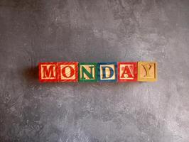A photo of a wooden block with the words monday written on it, styled in isolation with space for text.