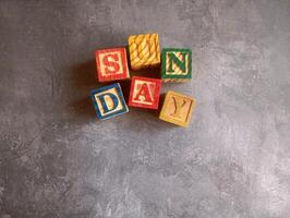A photo of a wooden block with the words sunday written on it, styled in isolation with space for text.