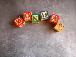 A photo of a wooden block with the words monday written on it, styled in isolation with space for text.