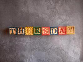 A photo of a wooden block with the words thursday written on it, styled in isolation with space for text.
