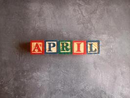 A photo of a wooden block with the words April written on it, styled in isolation with space for text.