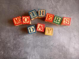 A photo of a wooden block with the words mothers day written on it, styled in isolation with space for text.