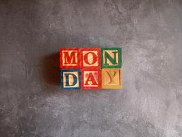 A photo of a wooden block with the words monday written on it, styled in isolation with space for text.