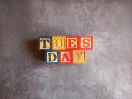 A photo of a wooden block with the words tuesday written on it, styled in isolation with space for text.