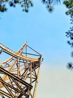 A roller coaster is seen from below with a blue sky in the background. The roller coaster is yellow and has a lot of metal photo
