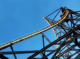 A roller coaster is seen in the distance with a clear blue sky in the background. The roller coaster is a large structure with a lot of metal and it is surrounded by a lot of empty space photo