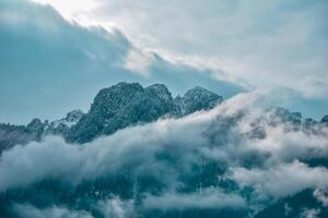 Majestic peaks pierce the azure sky, cloaked in a veil of ethereal clouds. This breathtaking mountain vista beckons us to pause and revel in nature's raw, untamed splendor. photo