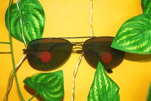 A pair of glasses suspended from a cable, decorated with leaves, and set against a yellow background. photo