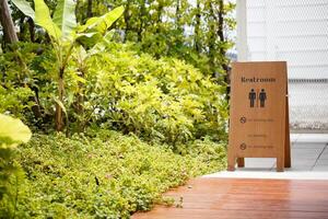 Restroom sign in lush garden setting, surrounded by vibrant greenery and plants, creating serene atmosphere. sign indicates no smoking areas, enhancing peaceful environment photo