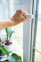 The hand holds the handle of a plastic double-glazed window, closing and opening the window with a rotary mechanism, the position of the handle for ventilation, micro-ventilation photo