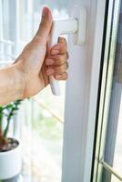 The hand holds the handle of a plastic double-glazed window, closing and opening the window with a rotary mechanism, the position of the handle for ventilation, micro-ventilation photo