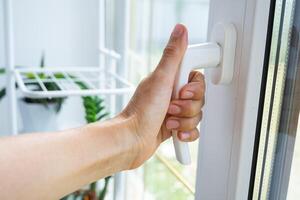 The hand holds the handle of a plastic double-glazed window, closing and opening the window with a rotary mechanism, the position of the handle for ventilation, micro-ventilation photo