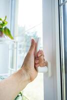 The hand holds the handle of a plastic double-glazed window, closing and opening the window with a rotary mechanism, the position of the handle for ventilation, micro-ventilation photo