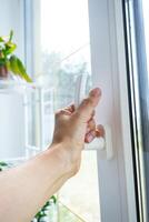 The hand holds the handle of a plastic double-glazed window, closing and opening the window with a rotary mechanism, the position of the handle for ventilation, micro-ventilation photo