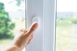 The hand holds the handle of a plastic double-glazed window, closing and opening the window with a rotary mechanism, the position of the handle for ventilation, micro-ventilation photo