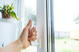 The hand holds the handle of a plastic double-glazed window, closing and opening the window with a rotary mechanism, the position of the handle for ventilation, micro-ventilation photo