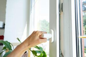 The hand holds the handle of a plastic double-glazed window, closing and opening the window with a rotary mechanism, the position of the handle for ventilation, micro-ventilation photo