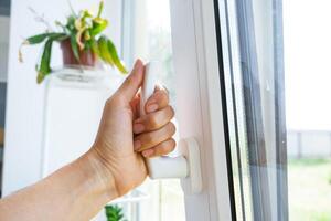 The hand holds the handle of a plastic double-glazed window, closing and opening the window with a rotary mechanism, the position of the handle for ventilation, micro-ventilation photo