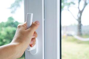 The hand holds the handle of a plastic double-glazed window, closing and opening the window with a rotary mechanism, the position of the handle for ventilation, micro-ventilation photo
