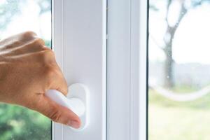 The hand holds the handle of a plastic double-glazed window, closing and opening the window with a rotary mechanism, the position of the handle for ventilation, micro-ventilation photo