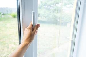 The hand holds the handle of a plastic double-glazed window, closing and opening the window with a rotary mechanism, the position of the handle for ventilation, micro-ventilation photo