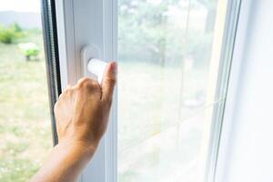 The hand holds the handle of a plastic double-glazed window, closing and opening the window with a rotary mechanism, the position of the handle for ventilation, micro-ventilation photo