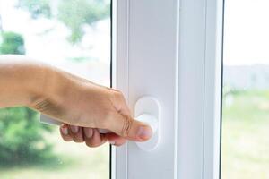 The hand holds the handle of a plastic double-glazed window, closing and opening the window with a rotary mechanism, the position of the handle for ventilation, micro-ventilation photo