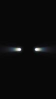 Front view of turning on the headlights in the car at night. Media. Abstract white lights of a car on a black background. Vertical . video
