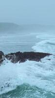 Beautiful waves break on rocks of rocky shore. Clip. Stone shore with storm waves in cloudy weather. Dramatic landscape of stone coast with beautiful splashes of waves video