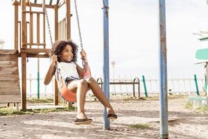 happy and smiling afro american girl playing on swing. fun and recreation concept. photo