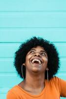 Portrait of cheerful Afro American girl smiling and looking at the camera. Happiness concept. Afro woman with orange sweater in front of green wall. photo