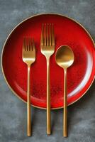 Elegant red plate set with golden fork and spoon arranged on a textured gray surface photo