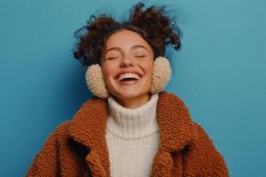 Young woman happily enjoying music while wearing cozy earmuffs against a blue background photo
