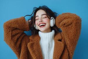 Young woman happily enjoying music while wearing cozy earmuffs against a blue background photo
