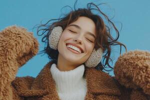 Young woman happily enjoying music while wearing cozy earmuffs against a blue background photo