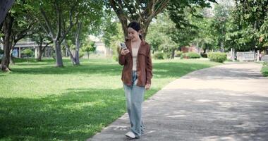 Handheld shot, Relaxed woman enjoying social media or chatting on mobile phone while walking in public park ,Holiday leisure activities video