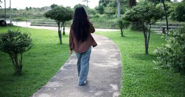 Handheld back view shot, Happy woman enjoys talking on her mobile phone while walking in a park. A holiday time surrounded by nature video