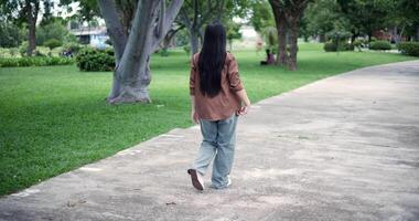 Handheld back view shot, Happy young woman enjoys a relaxing walk in a park, Enjoying the fresh air and the beauty of nature around her. video
