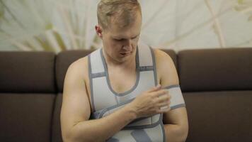 Painful, bored man with a broken arm wearing arm brace sitting on a sofa video