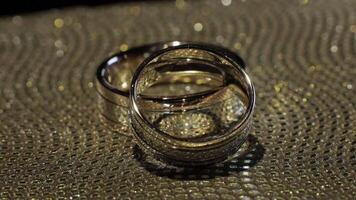 Wedding gold rings lying on shiny glossy surface. Shining with light. Close-up video